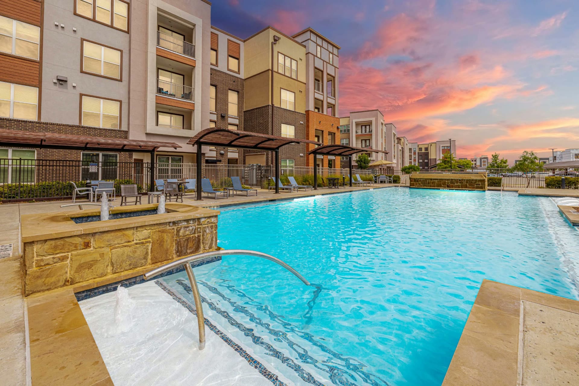 Apartment pool at twilight with pink sky and pergolas